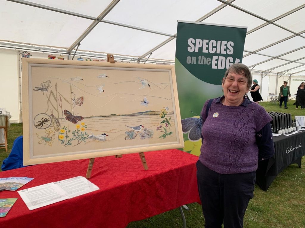 One of the Sutherland Stitchers stands beside their tapestry of endangered east coast species