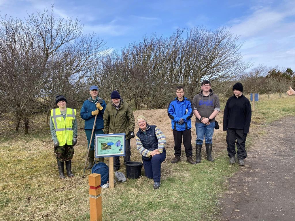 A group of volunteers smile for the camera in Dunnet Community Forest. They stand in front of a butterfly bank