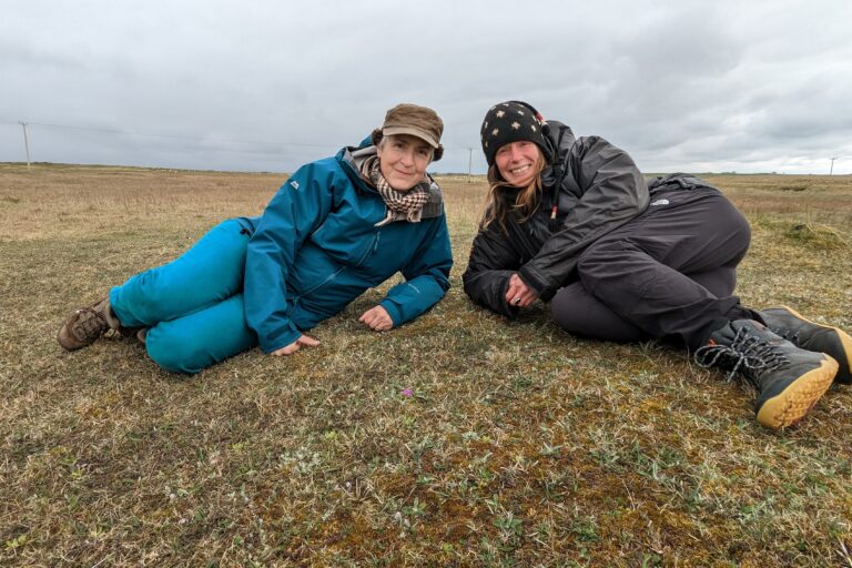 Louise and Sarah lie on the ground with a Scottish primrose