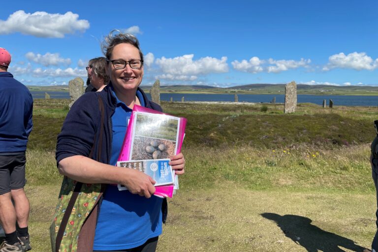 Sam at the Ring of Brodgar holding Species on the Edge information resources