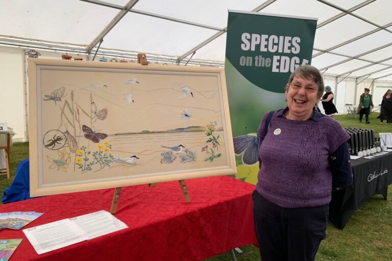 One of the Sutherland Stitchers stands beside their tapestry of endangered east coast species