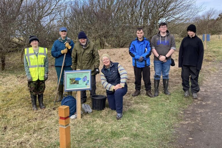 A group of volunteers smile for the camera in Dunnet Community Forest. They stand in front of a butterfly bank
